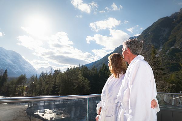 alpenbad-leutasch-im-fruehling-paar-steht-auf-balkon-und-blickt-auf-hohe-munde-aufnahme-gegen-die-sonne-1