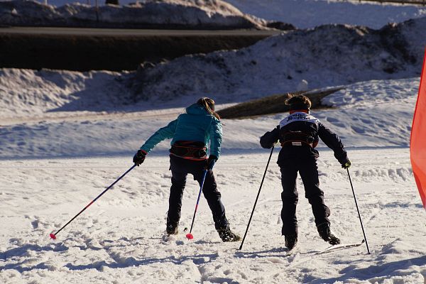 Zwei Kinder beim Langlaufen im Schnee mit Skistöcken, sonnige Winterlandschaft.