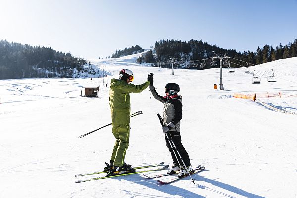 Zwei Skifahrer auf einer schneebedeckten Piste, die einander feiern.