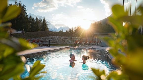 slider-alpenbad-leutasch-im-fruehling-paar-schaut-sich-an-im-pool-bei-sonnenuntergang-1