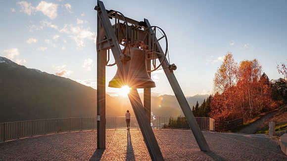 Friedensglocke im Herbst - Frau blickt ins Inntal beim Sonnenuntergang - Sonnenstern an der Glocke