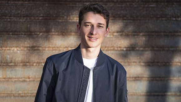 Junger Mann in dunkler Jacke vor Metallwand mit horizontalen Streifen