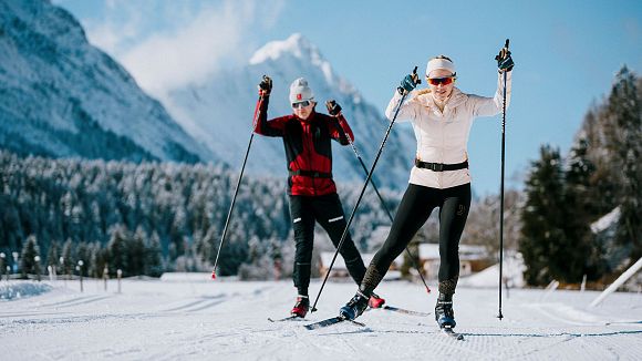 Zwei Personen beim Langlaufen in winterlicher Landschaft mit Schnee und Bergen.