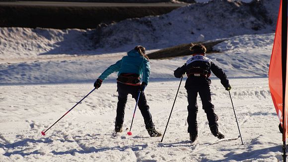 Zwei Kinder beim Langlaufen im Schnee mit Skistöcken, sonnige Winterlandschaft.