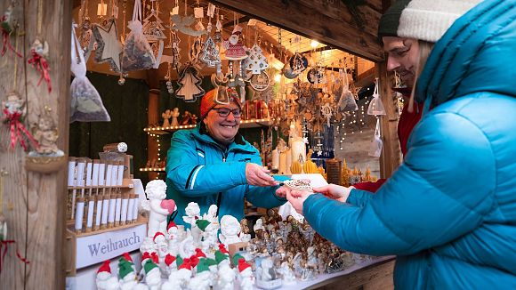 slider-weihnachtsmarkt-mit-menschen-paar-laesst-sich-ein-holzherz-beim-geschenkestand-reichen