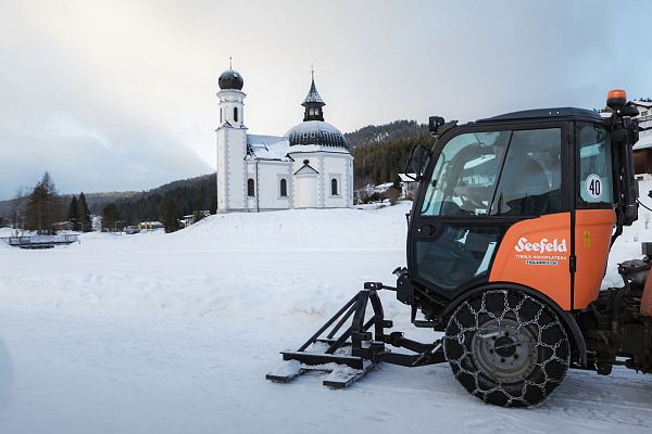 Winterlandschaft in der Region Seefeld mit Kirche und Schneeräumfahrzeug.