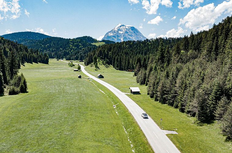 Eine malerische Landschaft mit grünen Wiesen, Bäumen und einer Straße unter einem blauen Himmel.