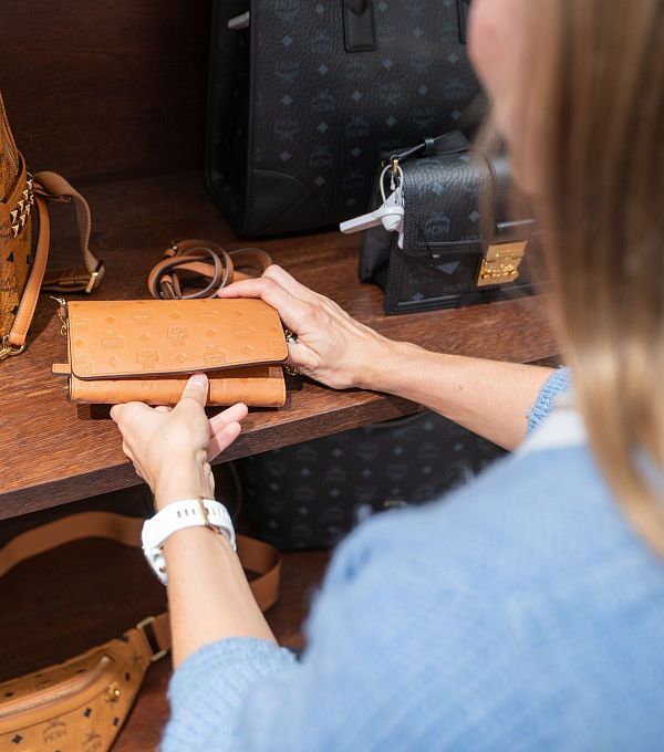 A person looking at a brown wallet on a shelf among various bags.
