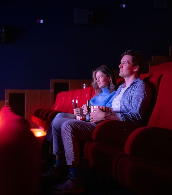 Zwei Personen sitzen in einem Kinosaal in roten Sesseln und schauen einen Film.