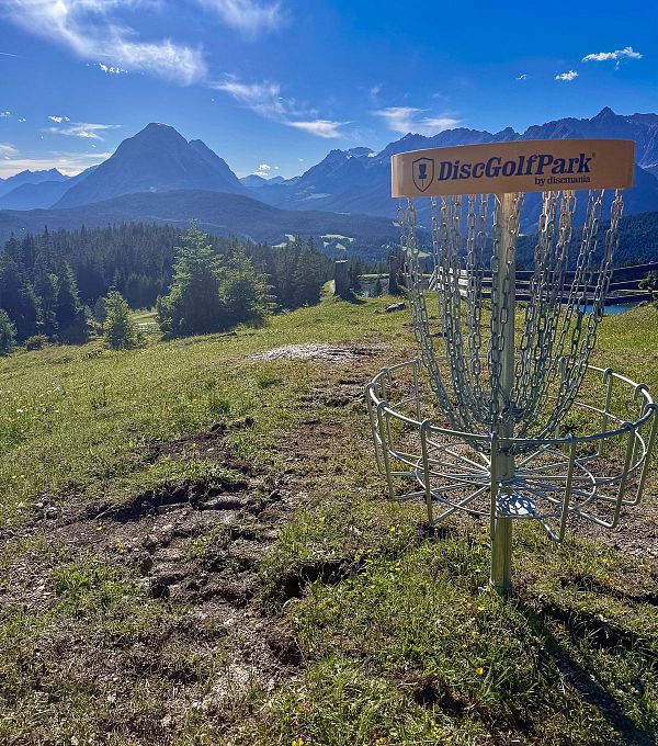 DiscGolfPark auf einer Wiese mit Bergen im Hintergrund.
