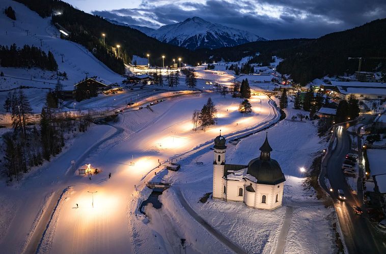 Verschneite Winterlandschaft bei Nacht in der Region Seefeld mit beleuchteter Kirche und Skipisten.