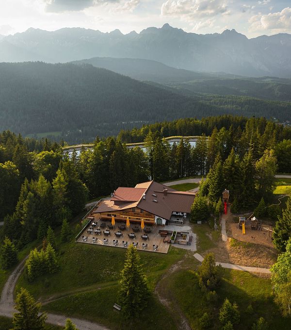 Immagine aerea di un edificio circondato da alberi e montagne, con un paesaggio collinare.