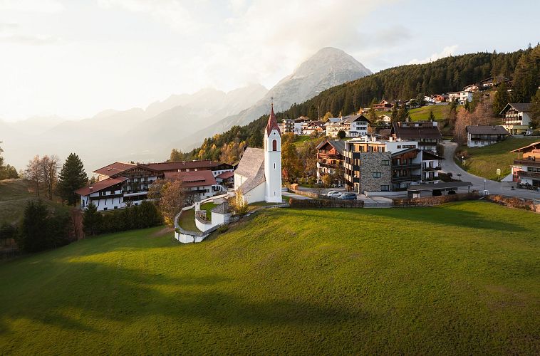 Drohnenaufnahme Mösern im Herbst_Kirche mit Hohe Munde bei Sonnenuntergangsstimmung