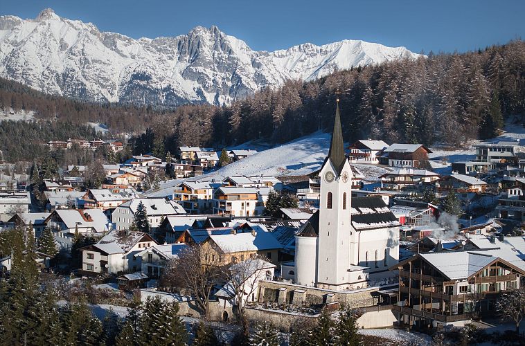 Drohnenaufnahme Reith im Winter - Kirche reingezoomt mit Wettersteingebirge im Hintergrund