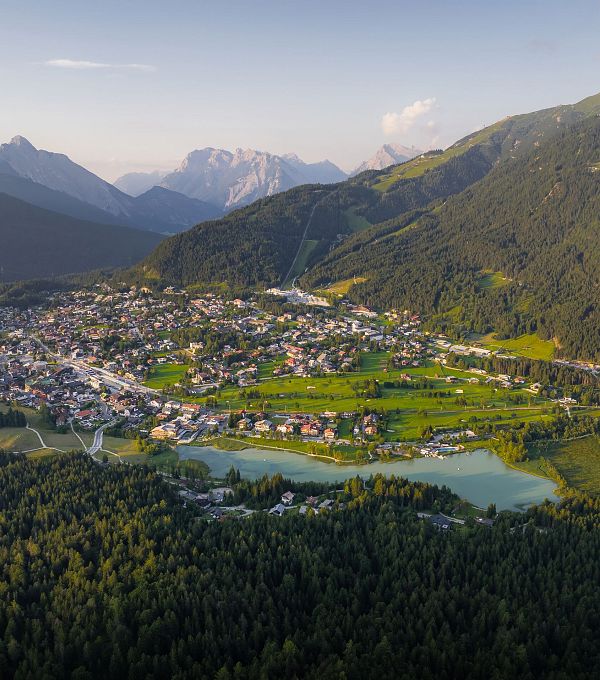 Luftaufnahme eines kleinen Dorfes in einem Tal, umgeben von Bergen und einem See.
