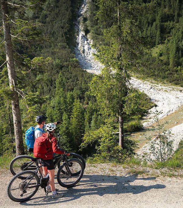 Zwei Radfahrer betrachten die Aussicht auf ein grünes Tal mit einem Fluss.