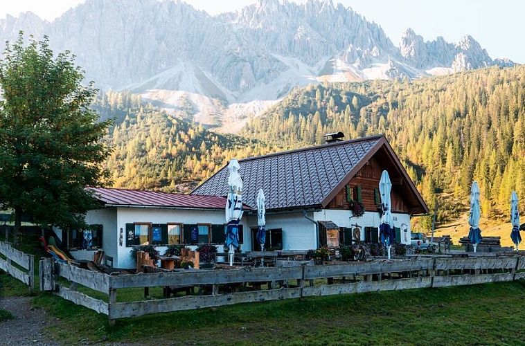 Berghütte mit rotem Dach, umgeben von Natur und Bergen.
