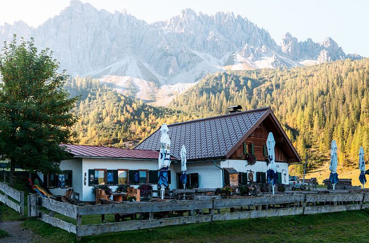 Berghütte in alpiner Landschaft vor majestätischen Bergen und grünem Wald. Perfekte Kulisse für Wandern und Naturerlebnis.