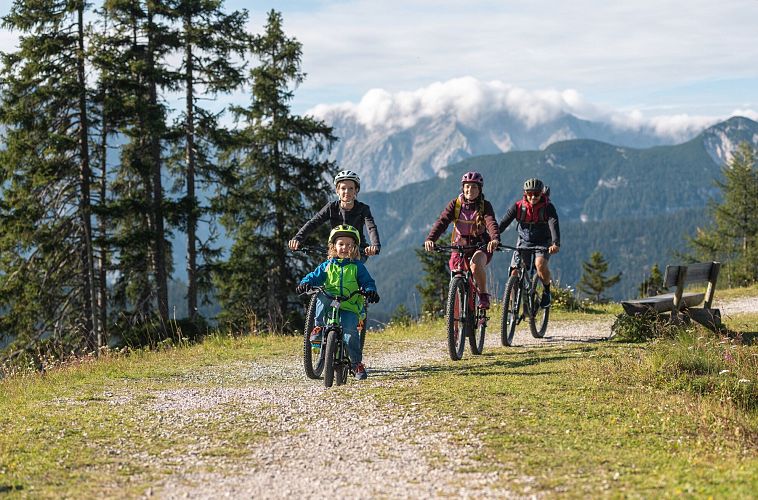 Familie beim Mountainbiken auf einem Pfad in der Region Seefeld, mit Bergen im Hintergrund.