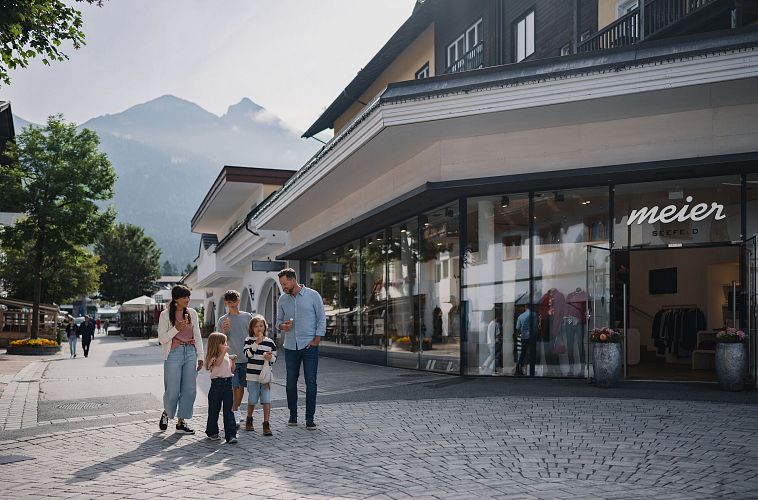 A family walking along a street with shops, surrounded by mountains.