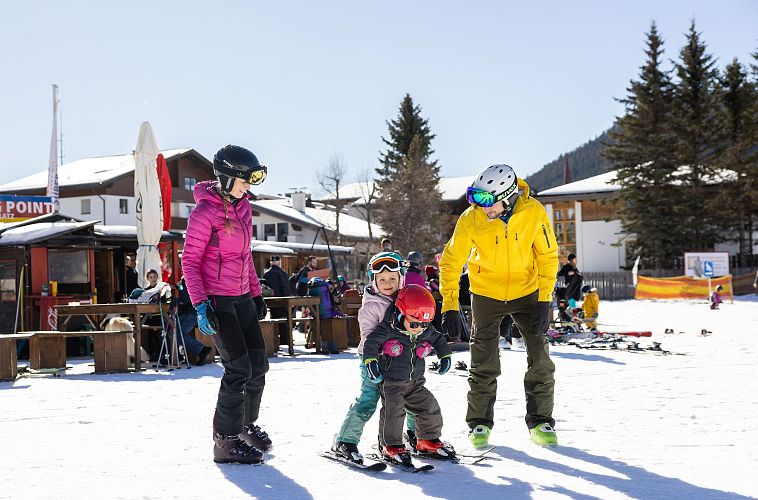Familie mit Kindern auf einem Schnee-Skiübungsgelände, Erwachsene helfen beim Skifahren.