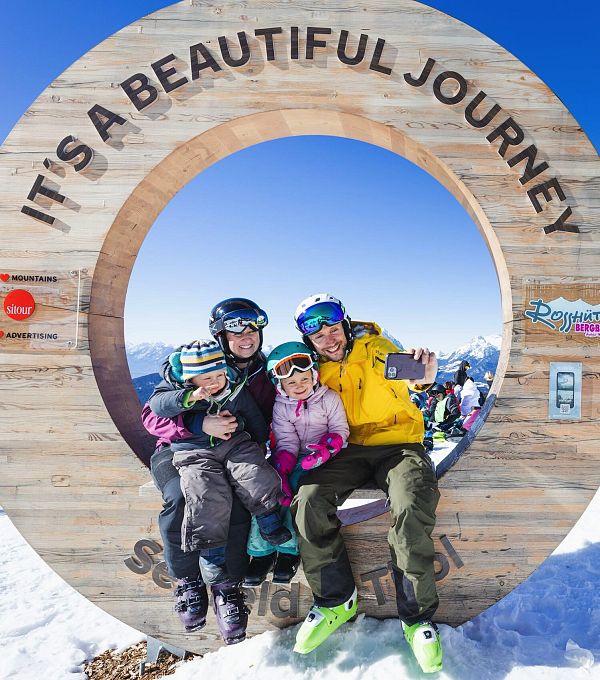 Gruppo di tre persone sorridenti all'interno di un cerchio di legno sulla neve.