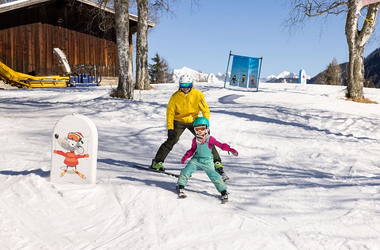 Kind und Erwachsener beim Skifahren in der Region Seefeld. Schneebedeckte Piste mit Gebirgslandschaft im Hintergrund.