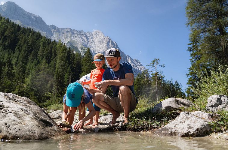 familien-weitwanderung-im-gaistal-familie-an-leutascher-ache-vater-und-tochter-holen-grosse-steine-aus-dem-wasser-tochter-bueckt-sich