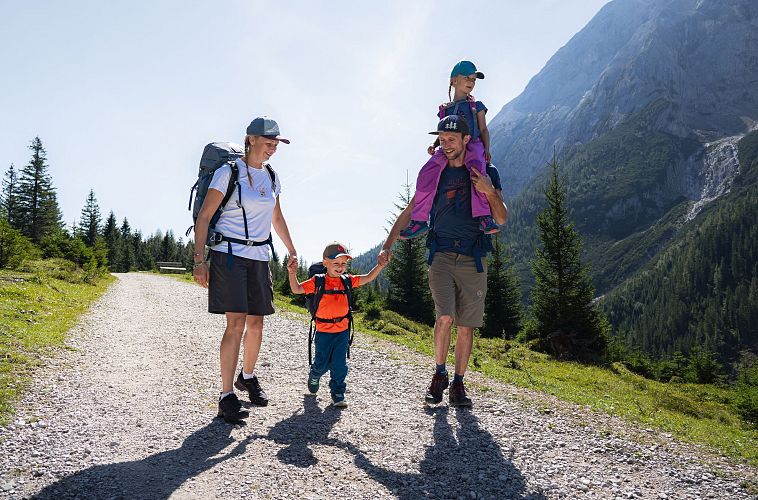 A family hiking on a sunny trail in the mountains with children and backpacks.