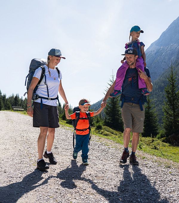 Familie wandert auf einem Weg durch eine Berglandschaft. Eltern und Kinder sind aktiv und fröhlich.