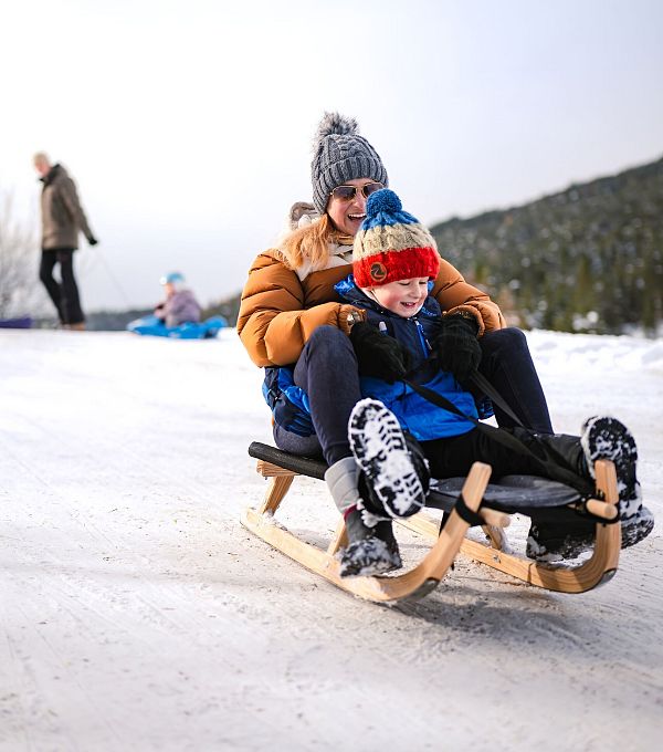 Eine Frau und ein Kind rodeln gemeinsam im Schnee.