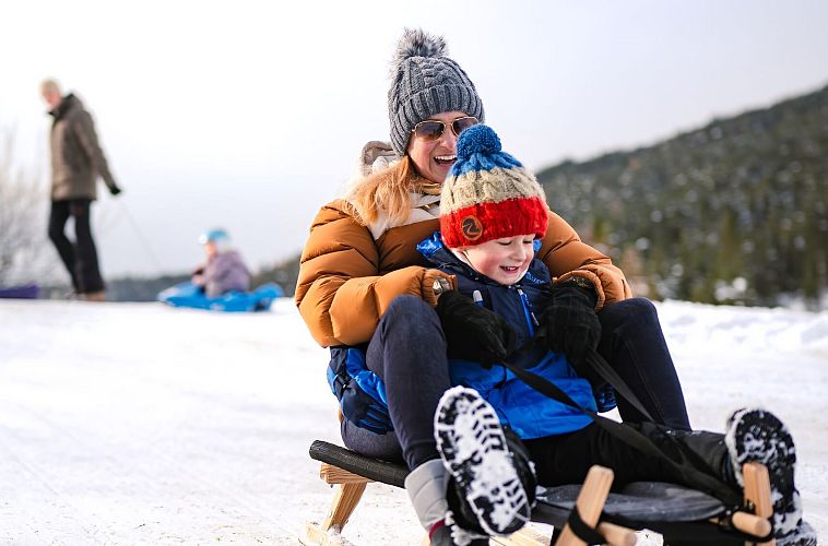 Mother and child sledding in snowy landscape, winter fun.