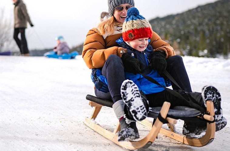 Eine Frau und ein Kind rodeln gemeinsam im Schnee.
