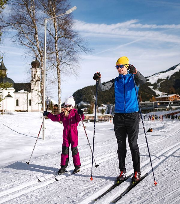 Mann und Kind auf Langlaufskiern auf Loipe, Kirche im Hintergrund, in der Region Seefeld.
