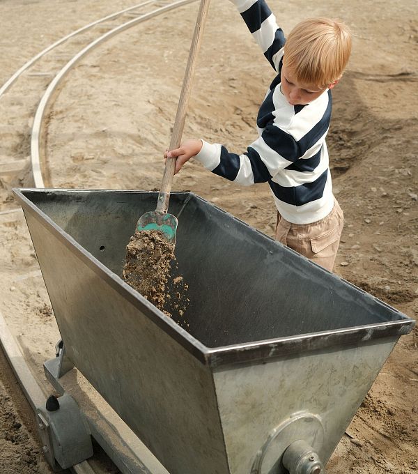 Ein Junge schaufelt Kies in eine große Metallschaufel auf einem Spielplatz.