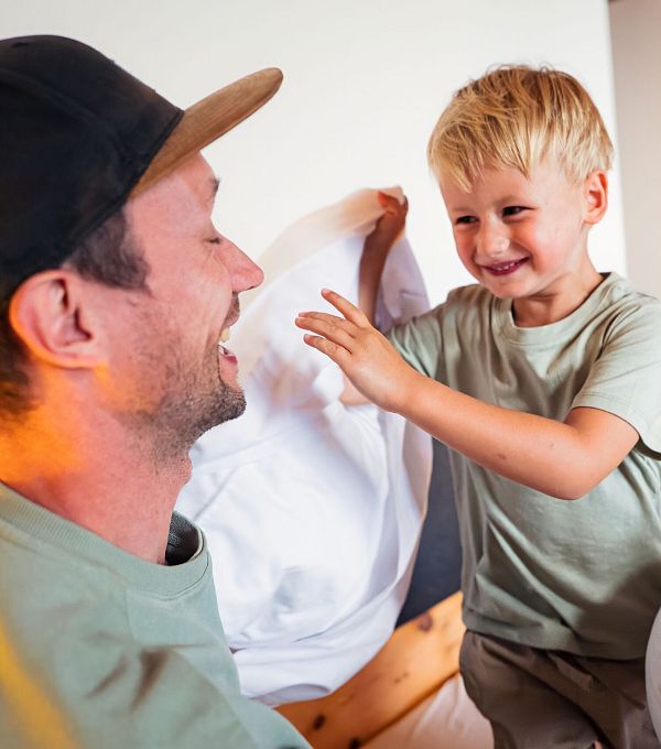 Vater und Sohn spielen mit Kissen in einem gemütlichen Raum.