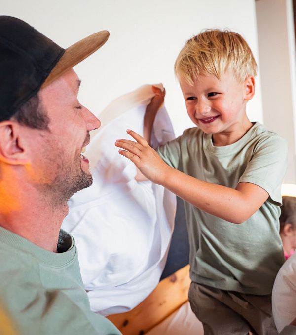 Vater und Sohn spielen mit Kissen in einem gemütlichen Raum.