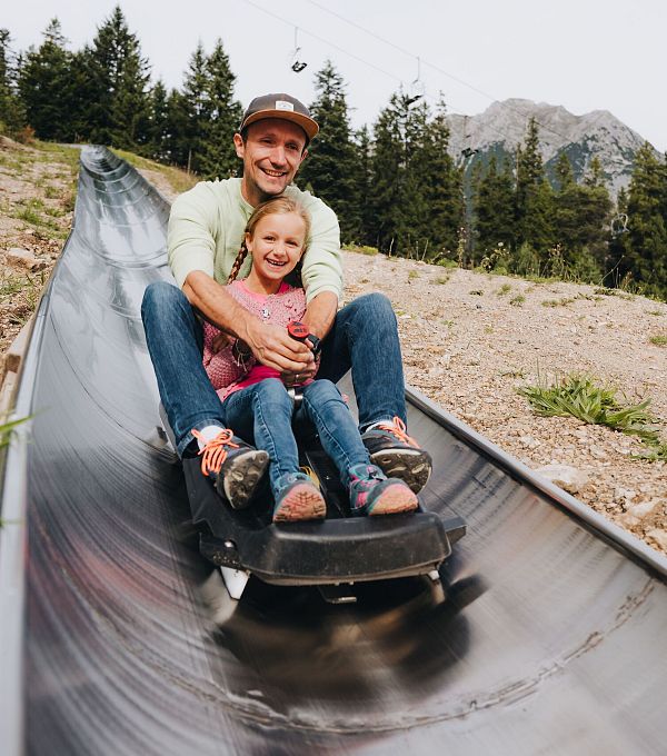 Ein Vater und seine Tochter fahren zusammen auf einer Sommerrodelbahn.