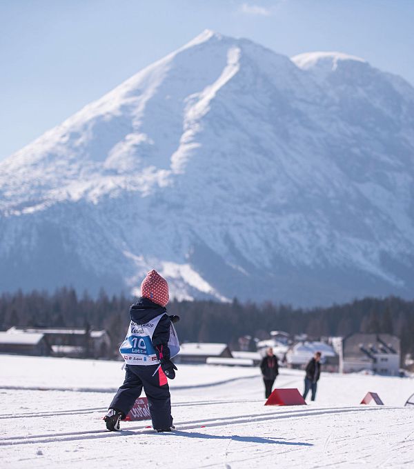 Kinder spielen im Schnee in der Region Seefeld, mit einer schneebedeckten Bergkulisse im Hintergrund.