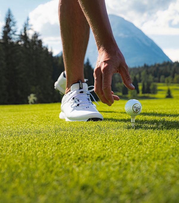 Ein Golfer hebt einen Golfball auf einem Platz mit einem Berg im Hintergrund.