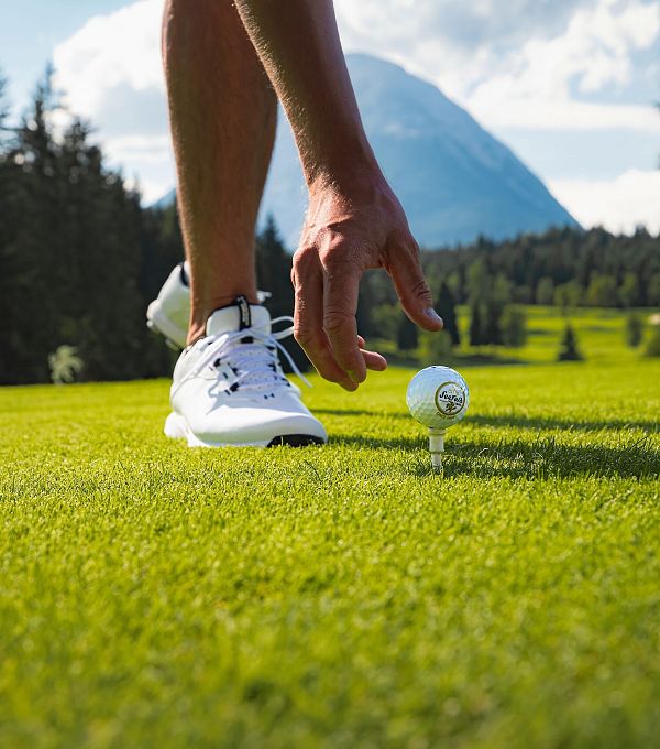 Ein Golfer hebt einen Golfball auf einem Platz mit einem Berg im Hintergrund.