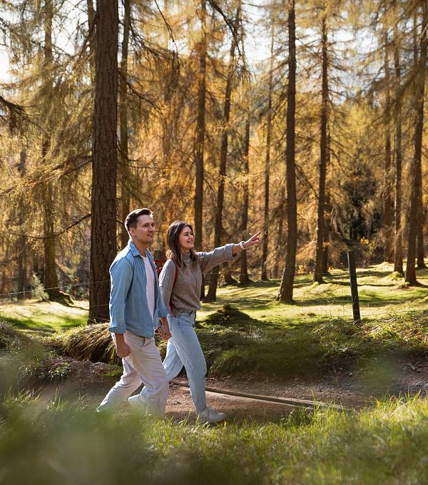 Herbstwanderung im Lärchenwald in Reith_Paar läuft durch Wald_Frau zeigt auf etwas (1)