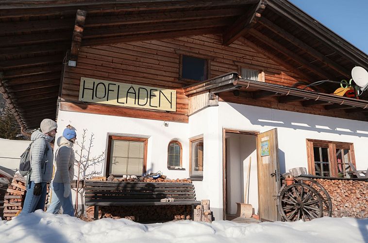 A farm shop named 'Hofladen' with snow outside and two people walking nearby.