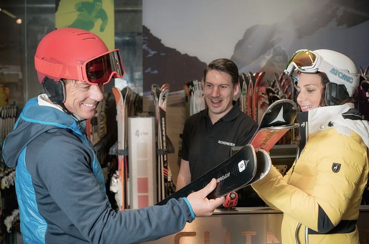 Ein Paar am Skiverleih mit einem Mitarbeiter, der Ski zeigt.