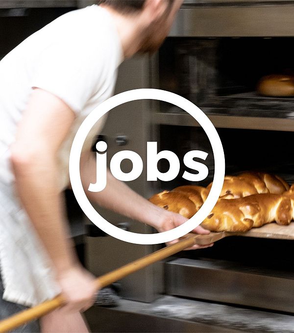 A baker placing bread in an oven with a wooden paddle.