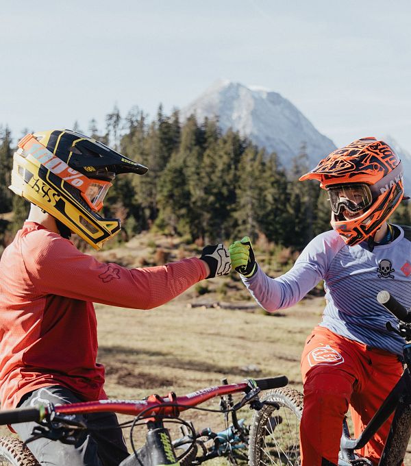 Zwei Kinder geben sich ein High Five auf ihren Mountainbikes in einer naturnahen Umgebung.
