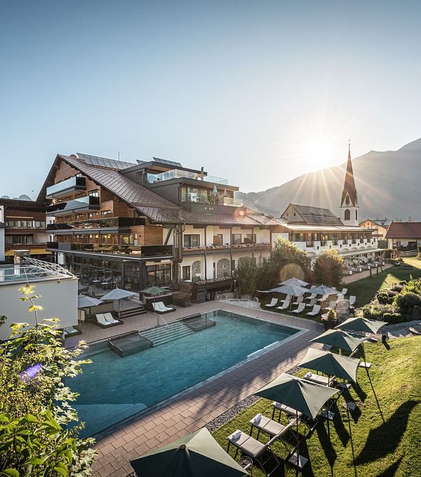 Stilvolles Hotel mit Pool und Sonnenliegen in einer Berglandschaft bei Sonnenaufgang.