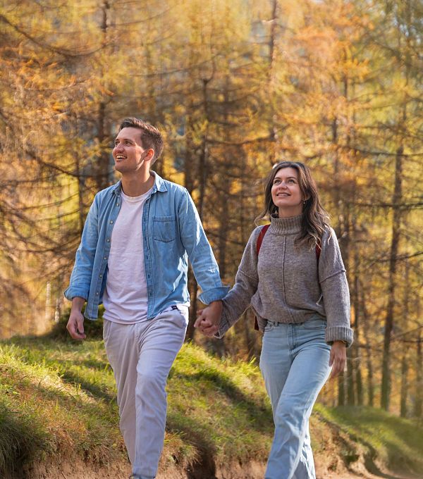 Ein Paar geht Hand in Hand durch einen Herbstwald mit goldenen Blättern.