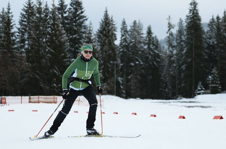 Skilangläufer in grüner Jacke fährt auf schneebedeckter Loipe, umgeben von Tannen.