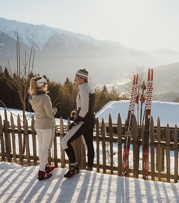 Zwei Langläufer im Schnee, im Hintergrund eine Berglandschaft und Skier.
